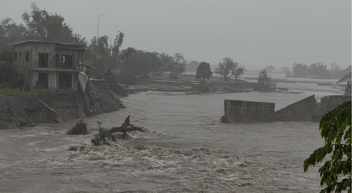 Raging floodwater cuts through Barangay Santo Cristo in Lubao beside damaged homes and collapsed concrete walls during heavy rain.