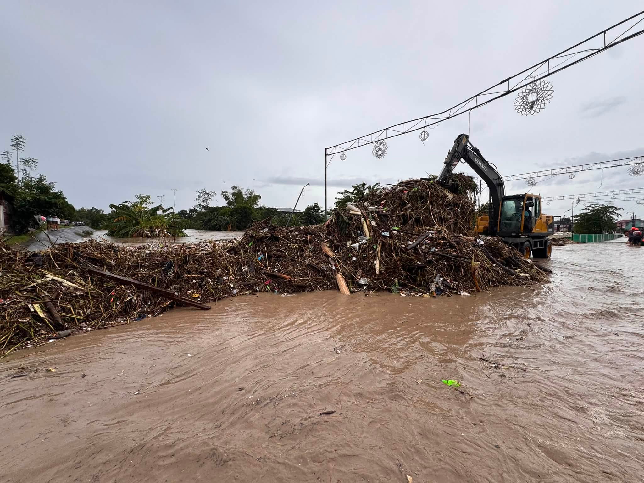 An excavator clears a large pile of storm debris from the flooded San Lorenzo Bridge area in Mexico.