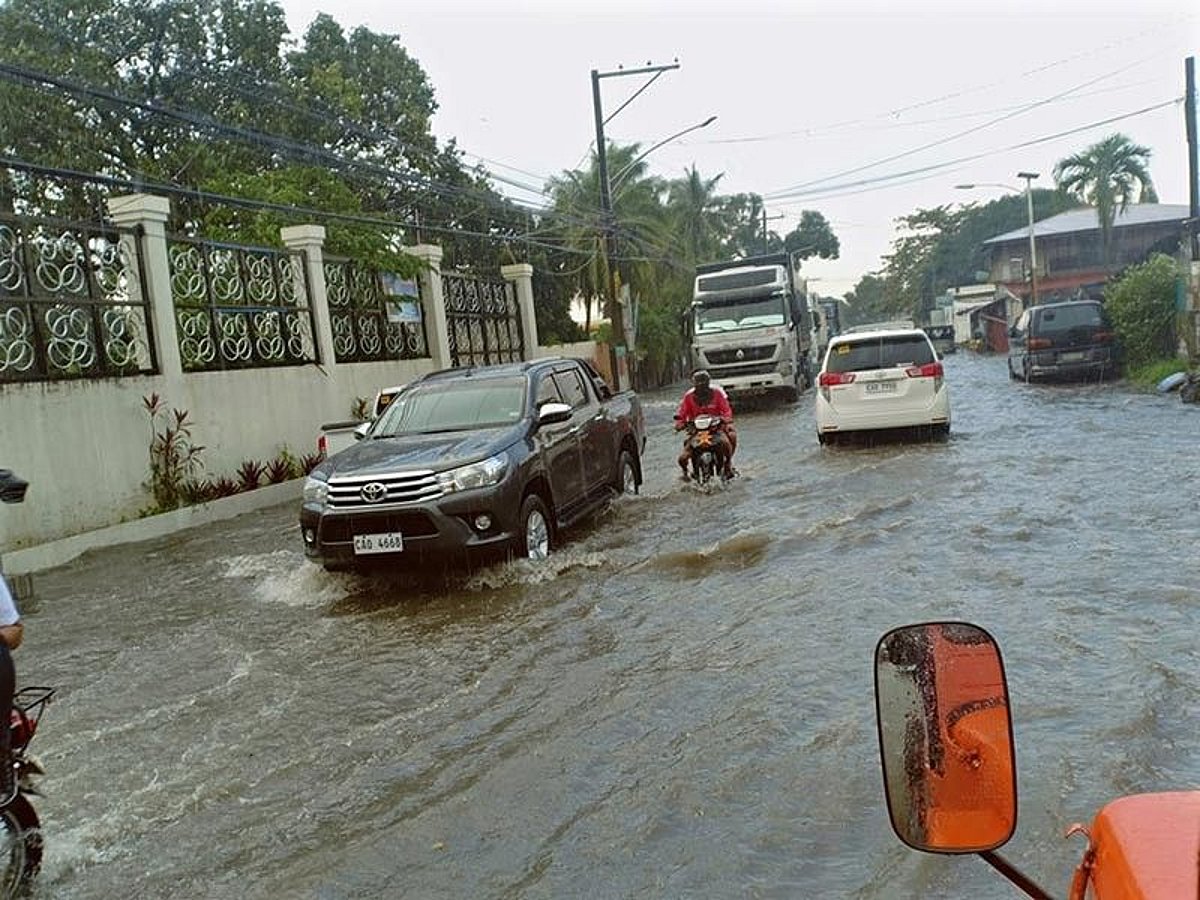 Cars, trucks and motorcycles move through deep floodwater covering the Porac-Angeles Road.